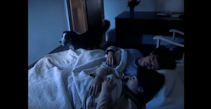 Una pareja duerme en su cama, mientras entra un perro a la habitacion