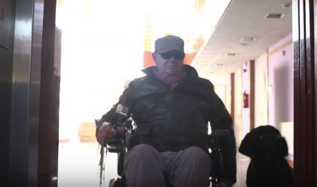 Hombre en silla de ruedas, espera subir a un ascensor junto a un perro de asistencia