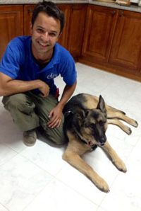 Educador canino apoyando la pierna izquierda en el suelo y a su izquierda se encuentra su perra Runa tumbada en el suelo, ambos mirando a la cámara
