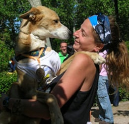 perro con una camiseta puesta y con una medalla colgada del cuello, en brazos de una corredora de canicross y mirándose a los ojos