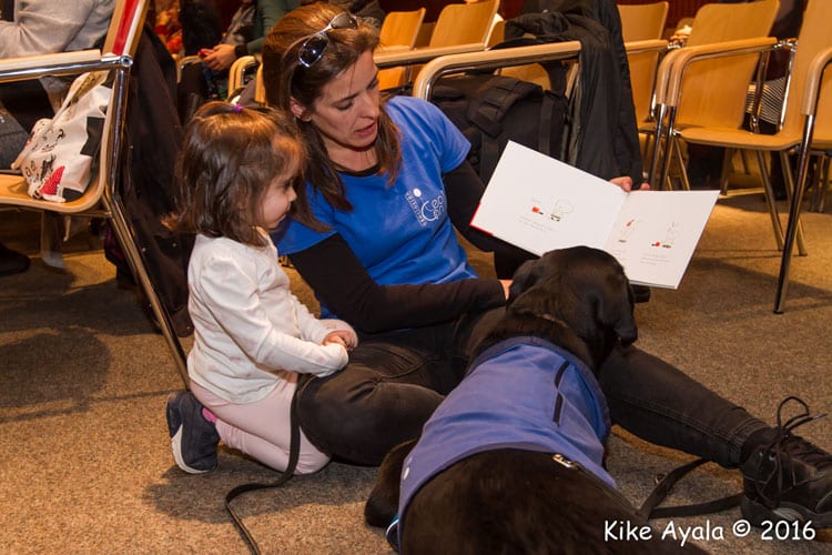 Educadora canina acompañada de un perro enseñando un libro a una niña
