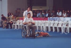 Dalmata en posición de quieto tumbado, al lado de la silla de ruedas con su entrenador Enrique Solís de LealCan