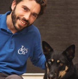 Sergio Mondéjar sonriente sentado y tocando con la mano izquierda el lomo de su perra Uva que está tumbada a su izquierda, ambos mirando a la cámara