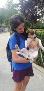 Educadora canina de pie mirando, sujetando y abrazando con los dos brazos el cuerpo de su perro Miko que está mirando ligeramente a la izquierda de la cámara